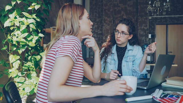 Two women having a serious discussion at a desk with a laptop in a consutation setting