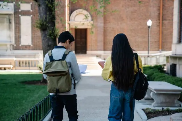 Two students with backpacks walking on a college campus.