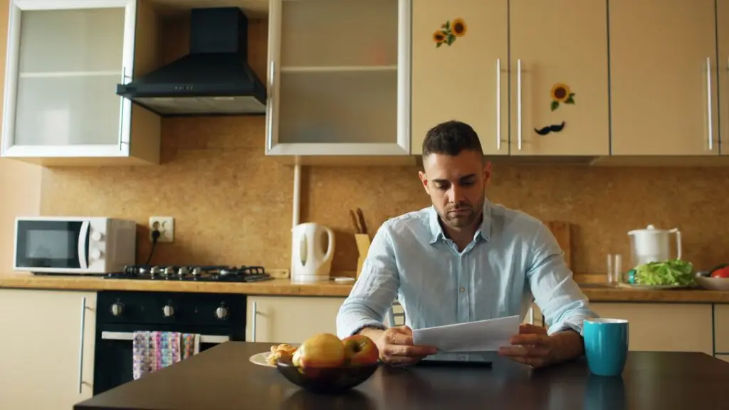 A parent seated at a kitchen table reading a school admissions document.