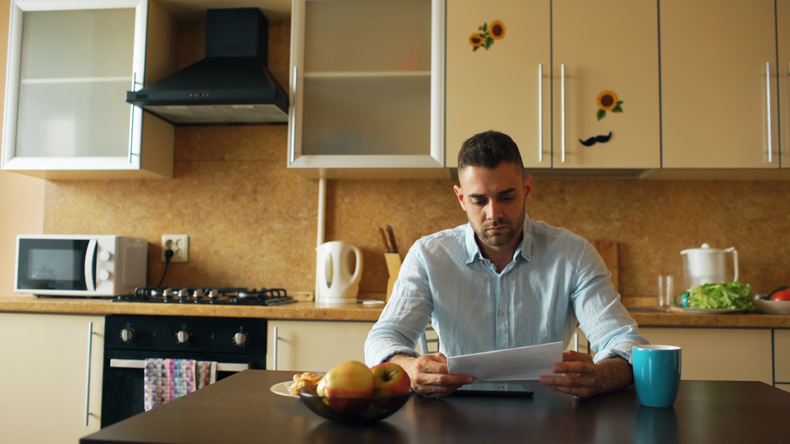 A parent seated at a kitchen table reading a school admissions document.