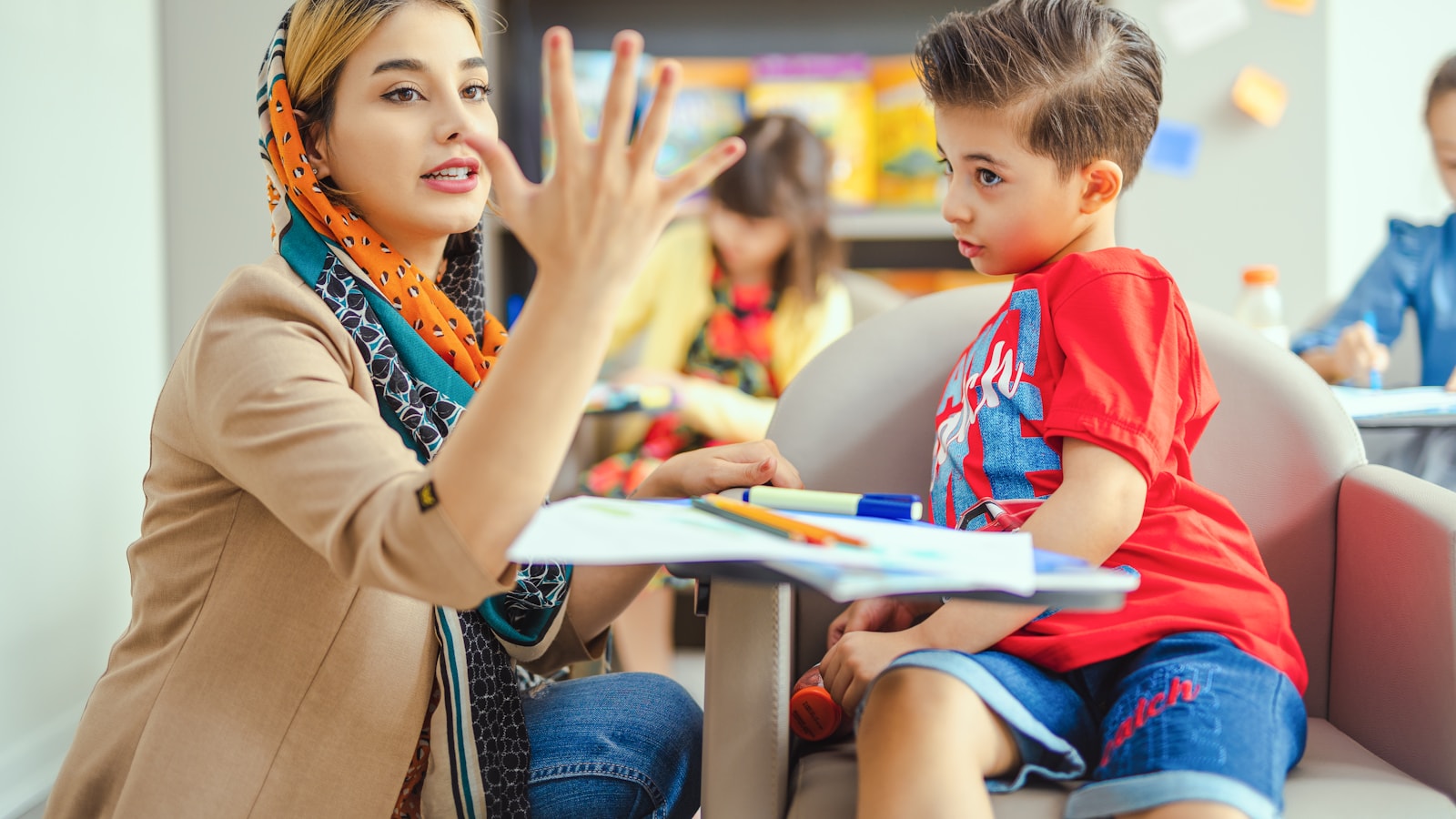 A teacher works one-to-one with a young student at a table in a primary classroom.