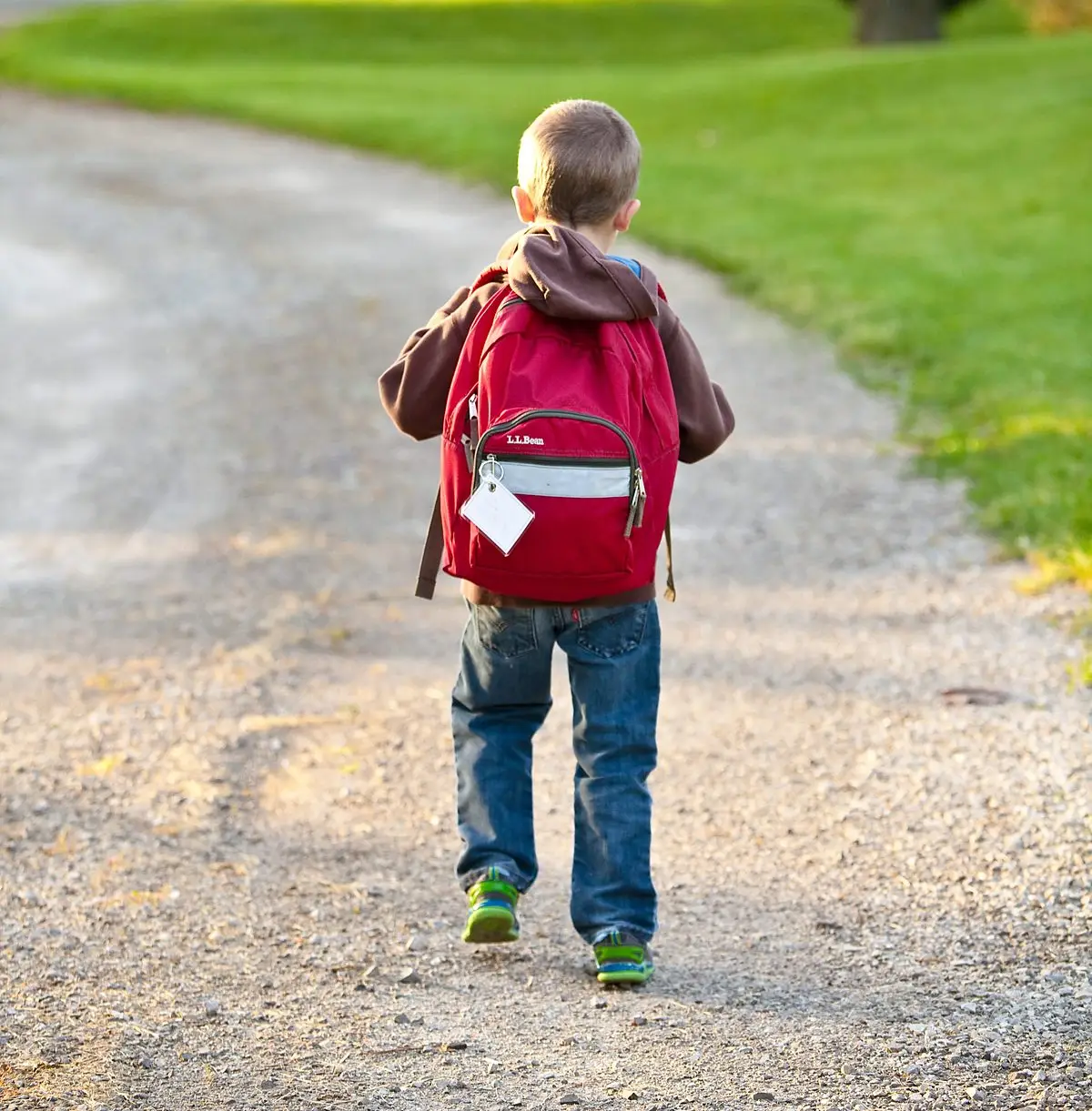 A young boy with a red backpack walking to school