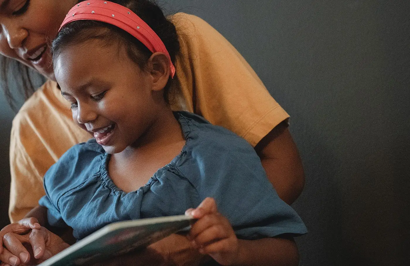 A child smiling while reading a book with a parent
