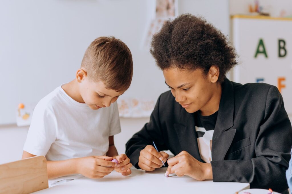 A learning support teacher works one to one with a young student on a classroom activity at a shared table