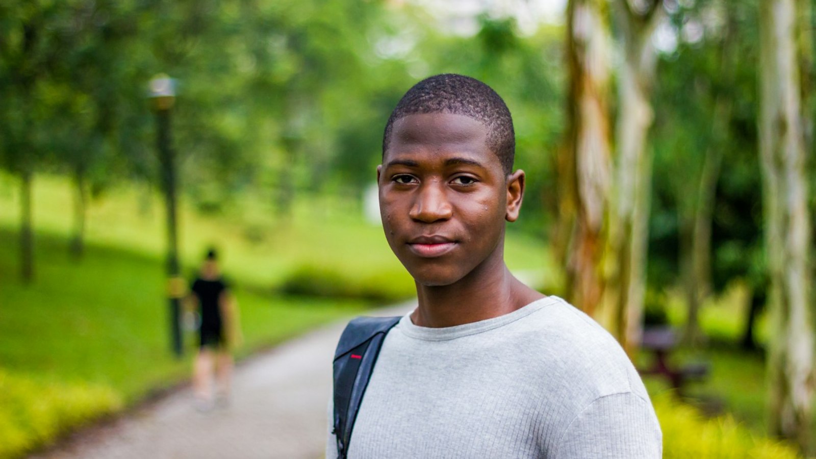 A student with a backpack standing on a tree-lined campus path