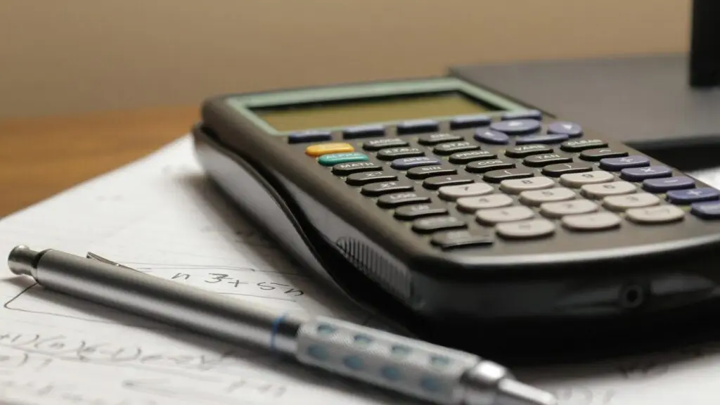 A calculator resting on printed figures and a pen