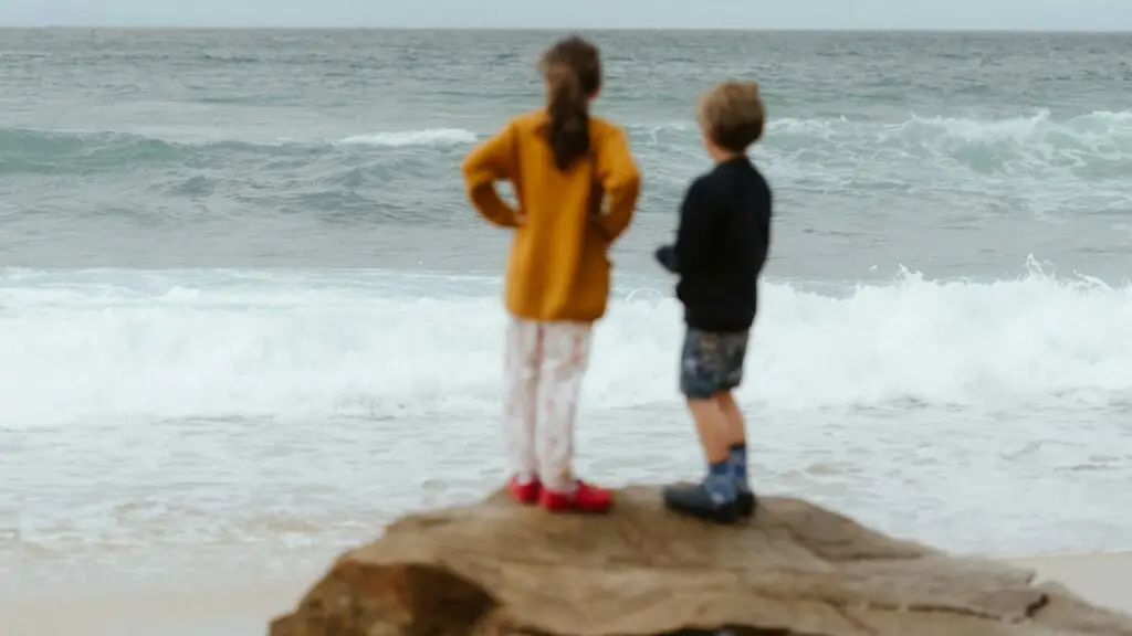 Two children standing on the rocks looking out at the surf on an Australian beach