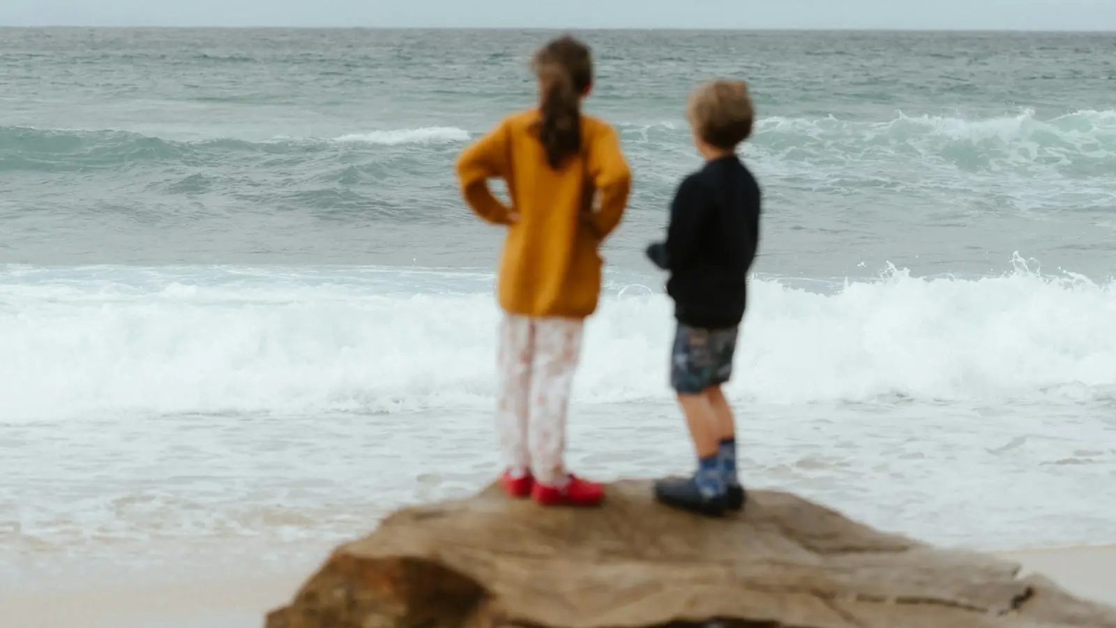 Two children standing on the rocks looking out at the surf on an Australian beach