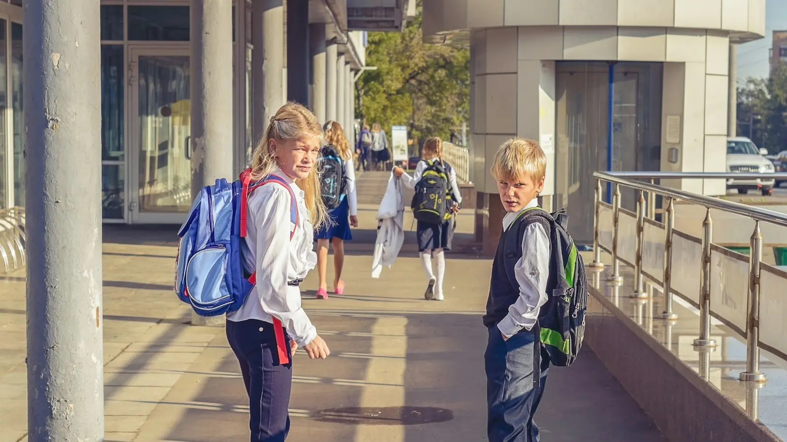 Two children with backpacks walking into school in the morning