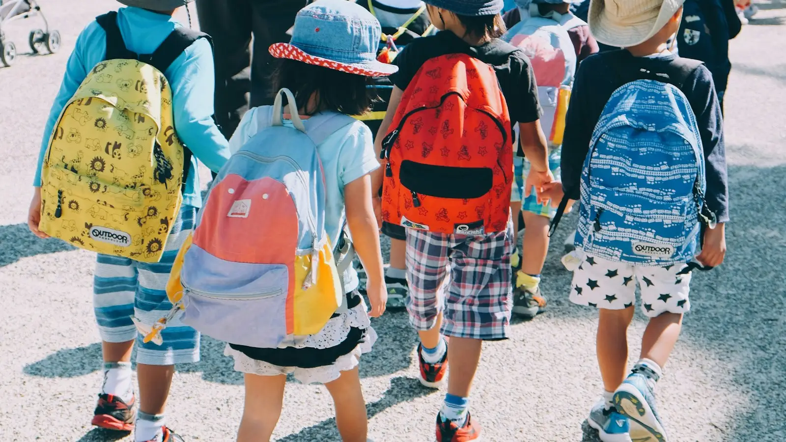 Young children in sun hats walking to school with their backpacks