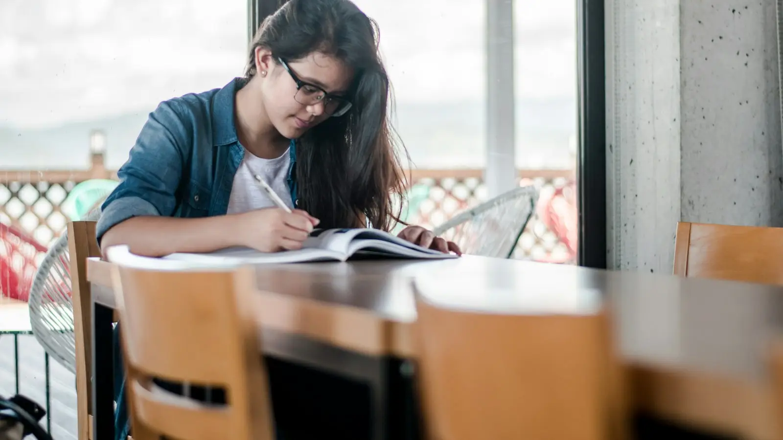 A high school student studying at a table by a window