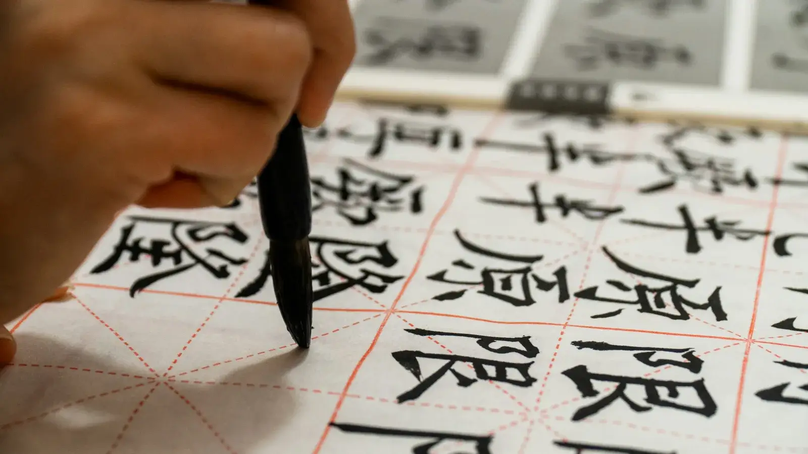 A hand practicing Chinese characters with a brush on grid paper