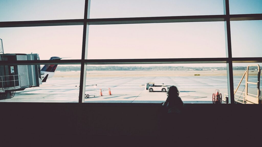 A child looking out of an airport window at the runway before a flight