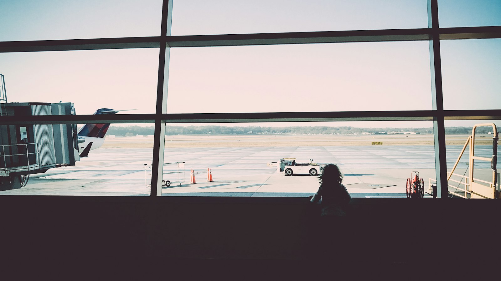 A child looking out of an airport window at the runway before a flight