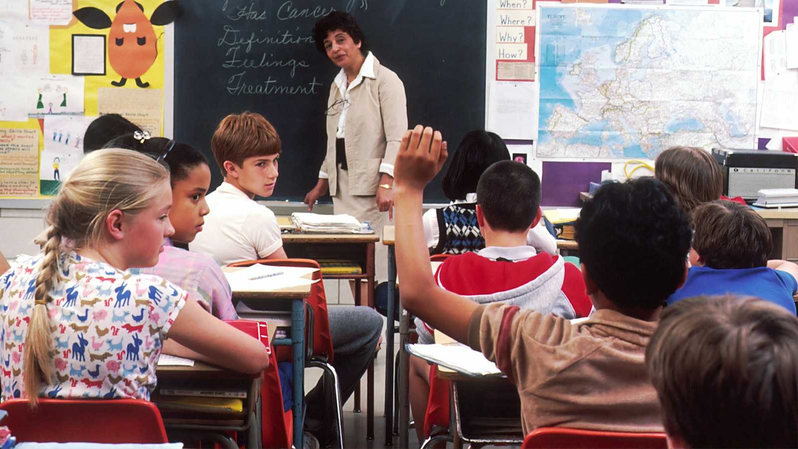 A teacher leans in to work with a group of young students in a classroom, the kind of individual attention that marks a supportive school.