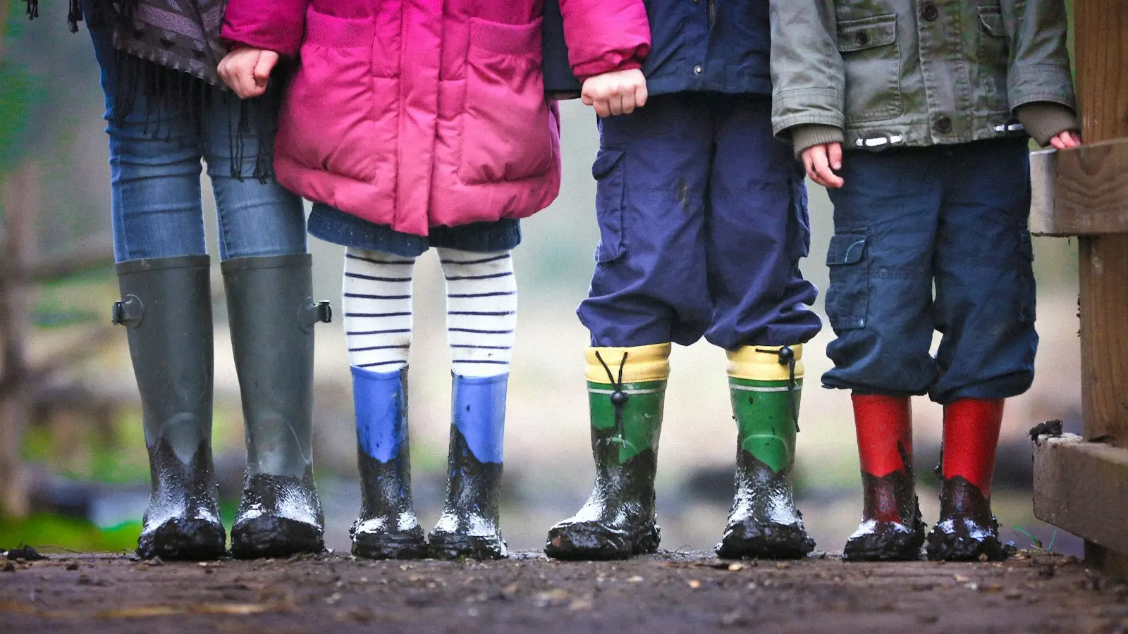 Four young children in wellington boots standing in a row after playing outdoors in England