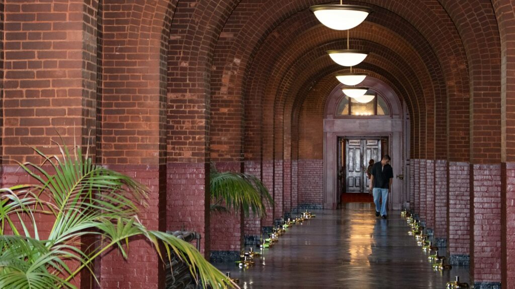 A long brick school corridor, lit by hanging lamps, leads toward an open doorway, the kind of space a family only gets a feel for on an in-person visit.